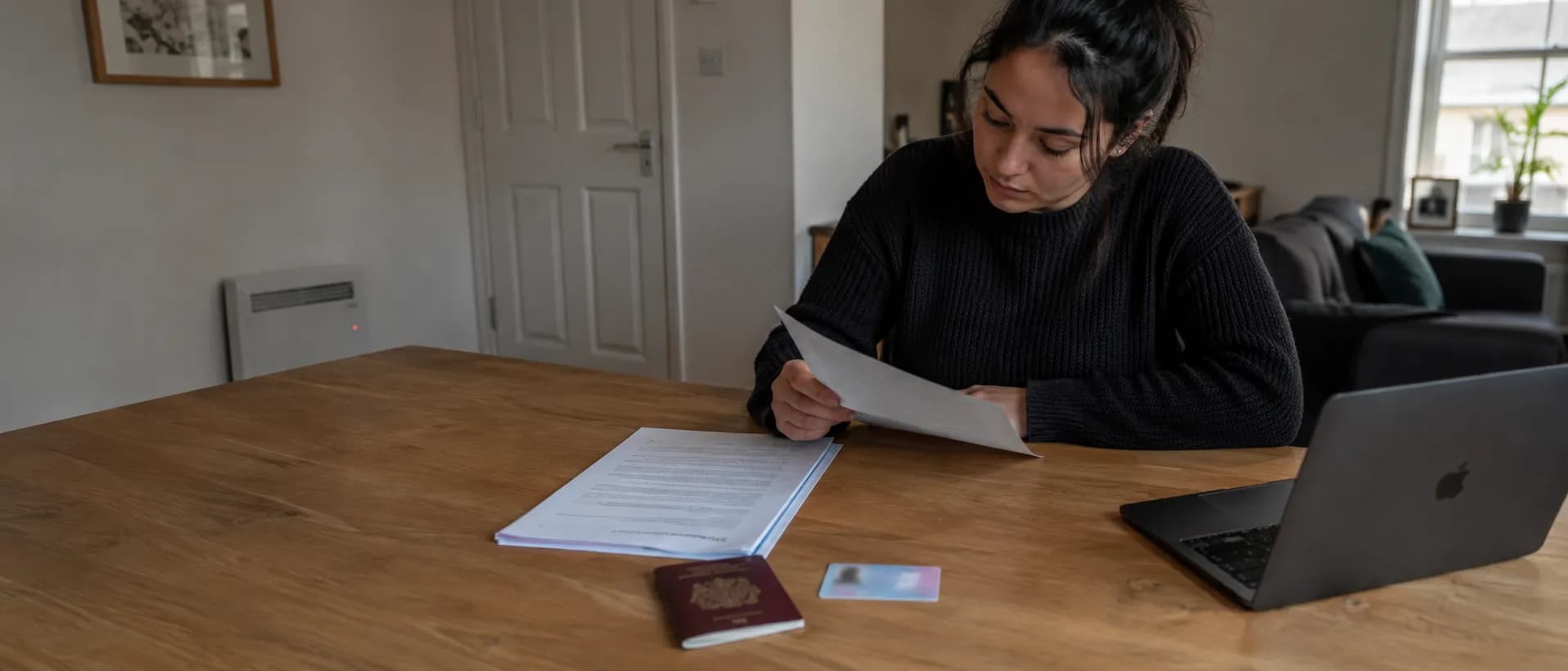 A recent graduate reading through a stapled employment contract at a dining table, with a passport and biometric residence permit card laid out alongside.