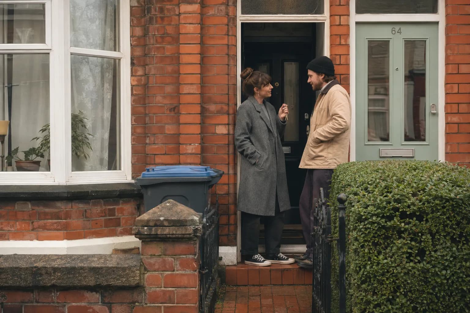 A couple holding the keys to their first UK home outside a red-brick terraced house.